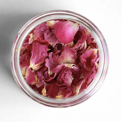 Glass jar filled with pink rose petals on a light gray background