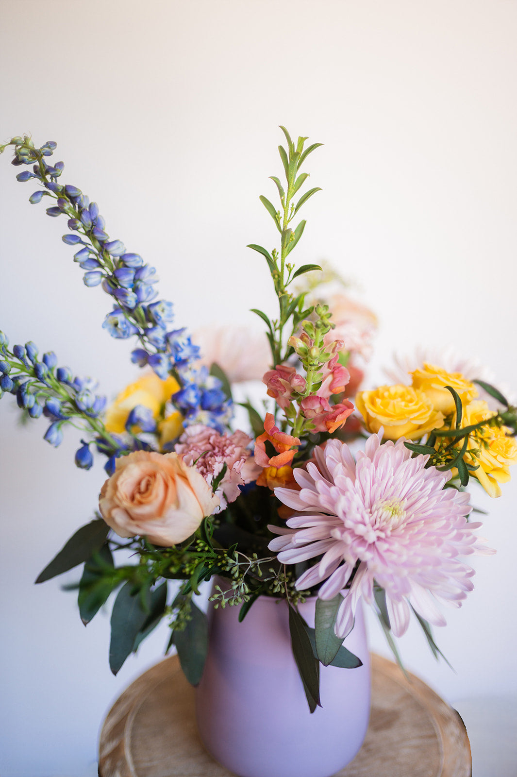Floral arrangement in a pink vase on a wooden surface with a white background