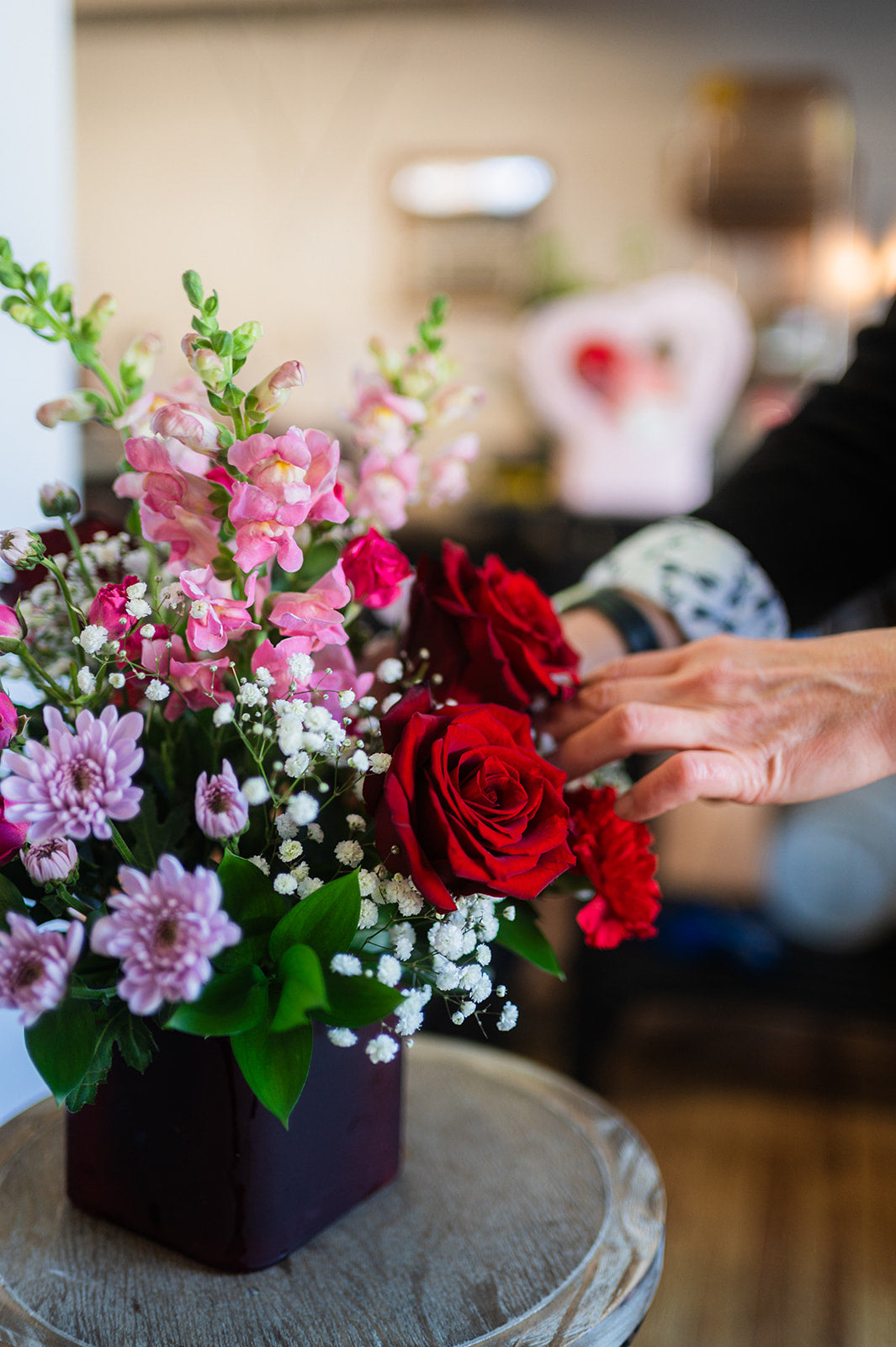 Hand reaching towards a bouquet of flowers on a table with a blurred background