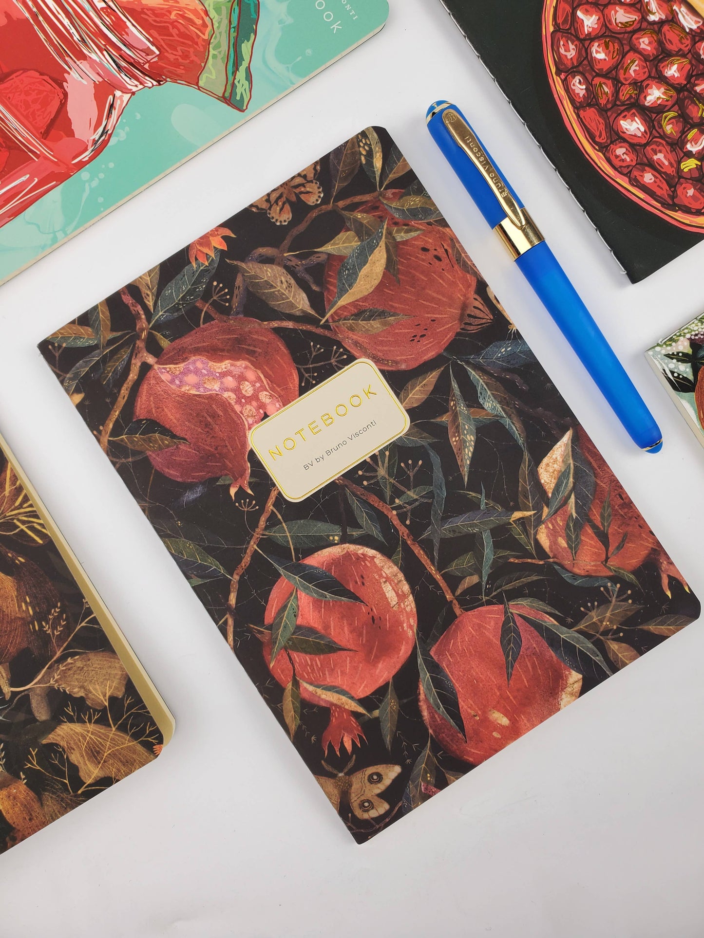 Notebook with pomegranate design, pen, and colorful cards on a white surface