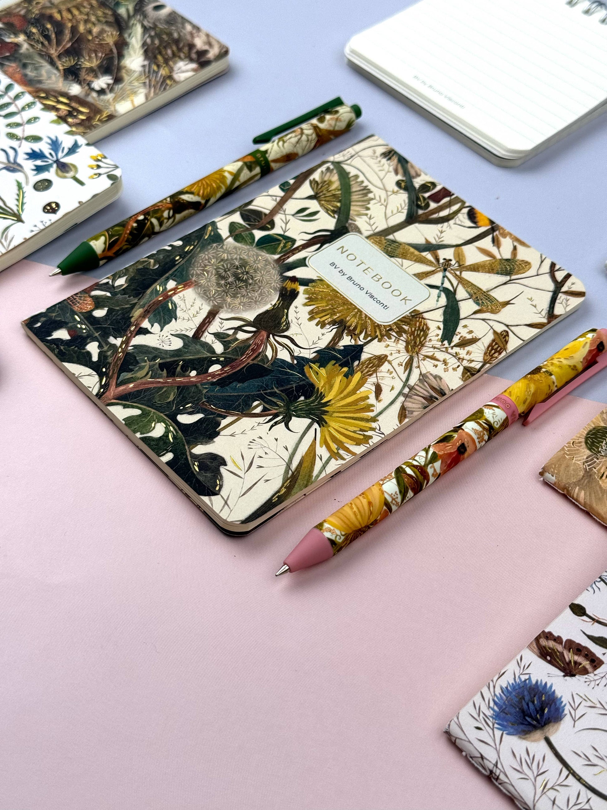 Notebooks with floral designs and matching pens on a light pink surface