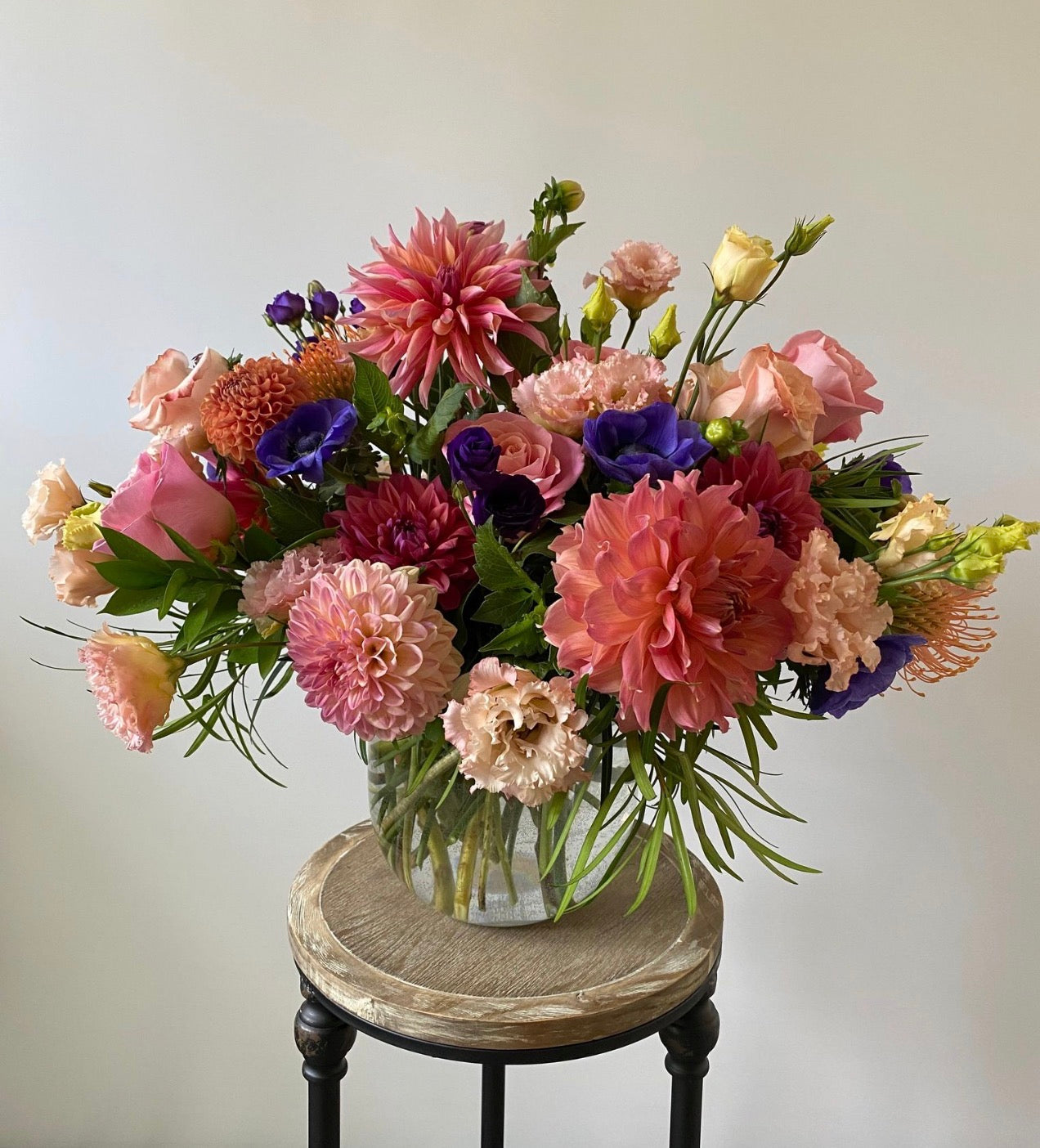 Colorful flower arrangement in a vase on a wooden stool against a plain background