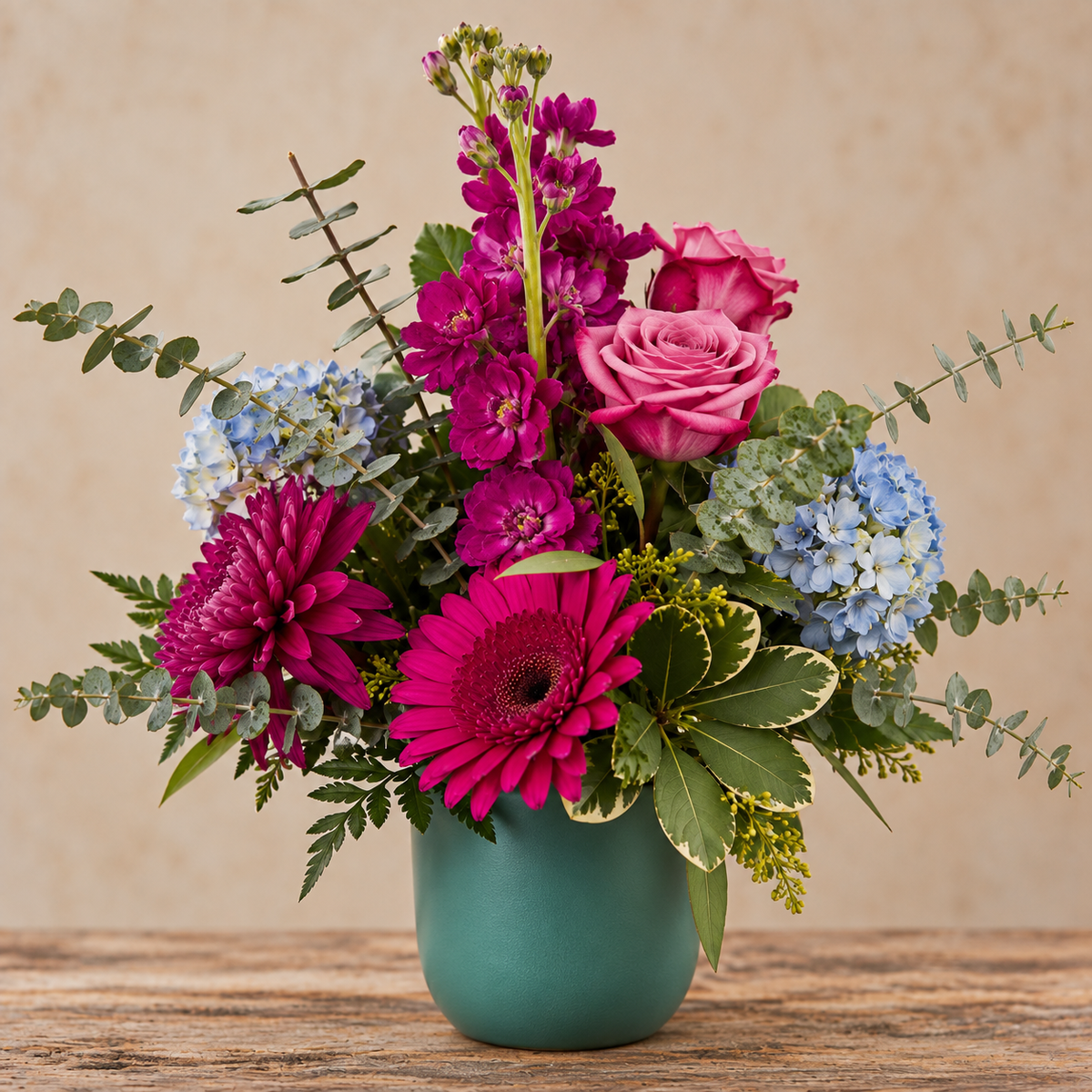 Fuchsia & Fabulous floral arrangement featuring lavender roses, fuchsia stock flowers, blue hydrangea, purple cremons, spiral and seeded eucalyptus, designed in a teal ceramic planter.