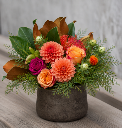 Harvest Cottage fall floral arrangement featuring peach roses, coral dahlias, rich seasonal blooms, magnolia leaves, and textured greenery in a rustic brown ceramic container.