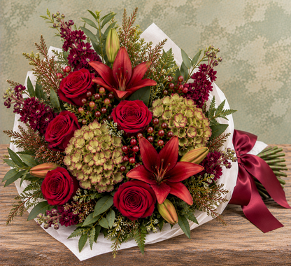October Meadow Wrapped Bouquet with deep red roses and lilies, antique green hydrangea, burgundy stock, hypericum berries and seasonal greenery, wrapped in white parchment with a burgundy satin ribbon